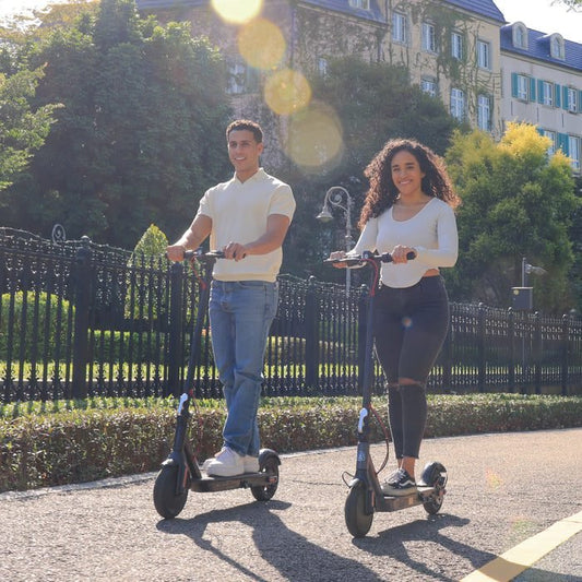 Two people riding electric scooters on a sunny day in an urban park.