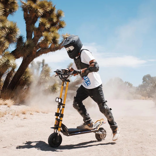 Person riding a scooter in a desert setting with Joshua trees.