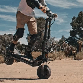 Person riding an electric scooter in a desert landscape with trees and clear sky.