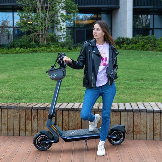 Woman standing next to an electric scooter on a wooden deck with grass and building in the background