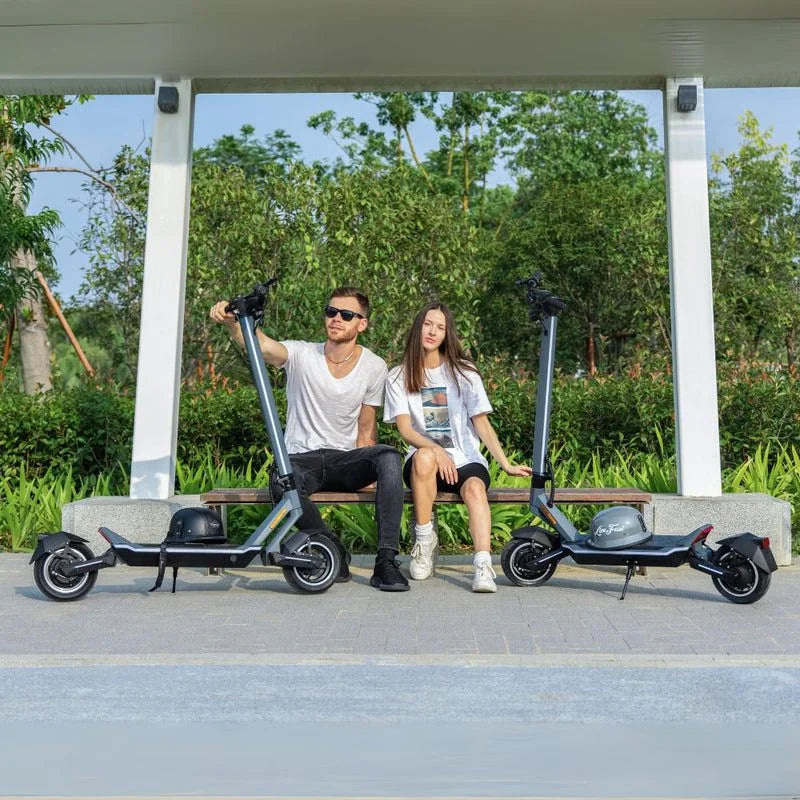 Two people sitting on a bench with electric scooters in a park setting