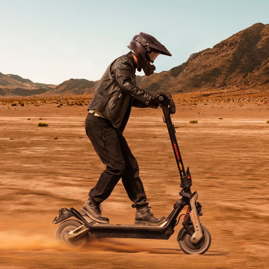 Person riding a scooter in a desert landscape with mountains in the background