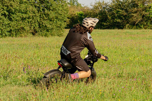 Person riding a balance bike in a grassy field with trees in the background