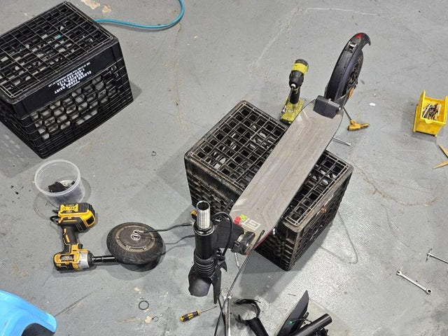 Electric scooter taken apart on the floor of a Wilson's repair shop, with tools