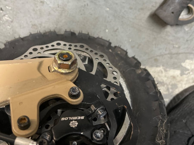 Brake caliper and disc on an electric scooter wheel during a safety check at a Wilson's shop