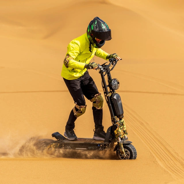 Person riding a sandboard in the desert wearing a yellow jacket and helmet.