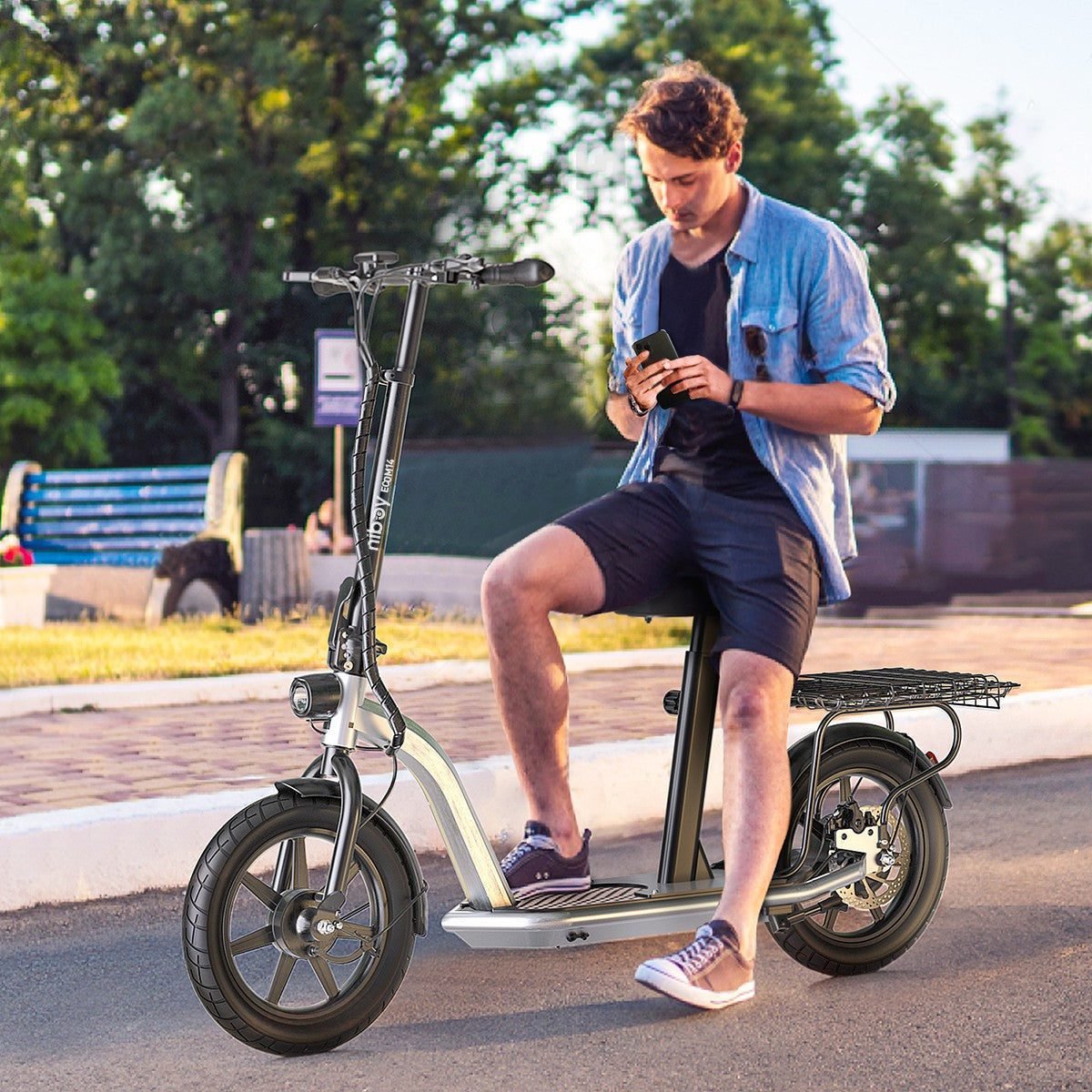 Man using a smartphone while sitting on an electric scooter in a park-like setting.