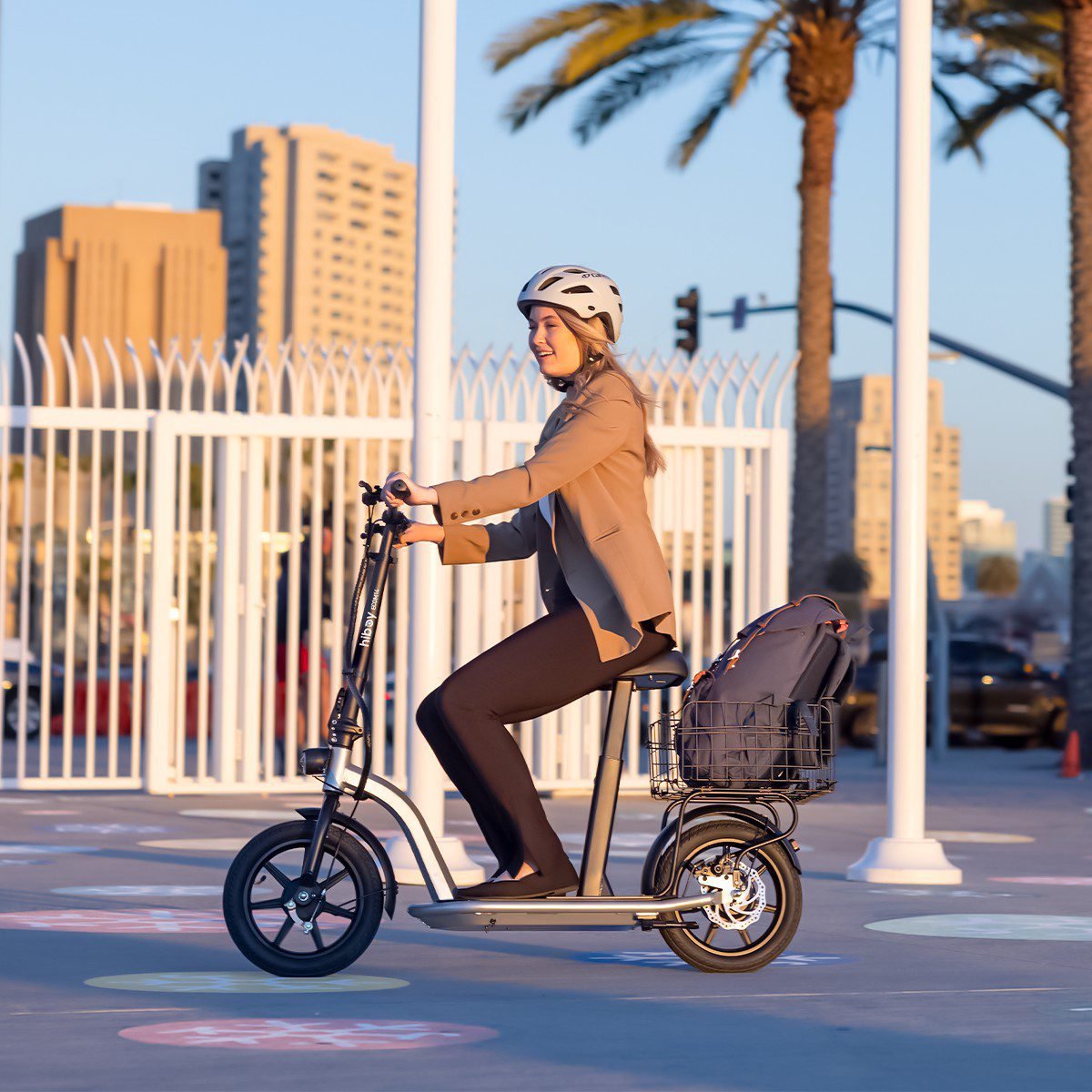 Person riding an electric scooter with a helmet on a city street with palm trees in the background.