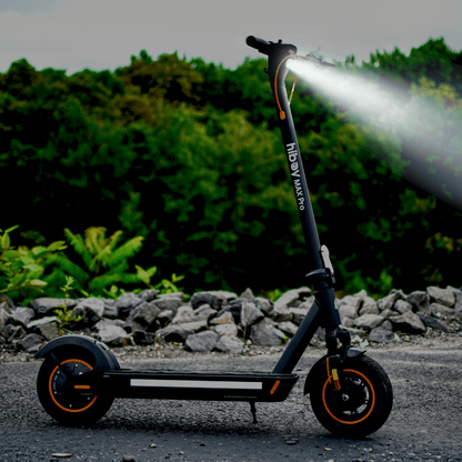 Electric scooter with a light on, parked on a road with greenery in the background