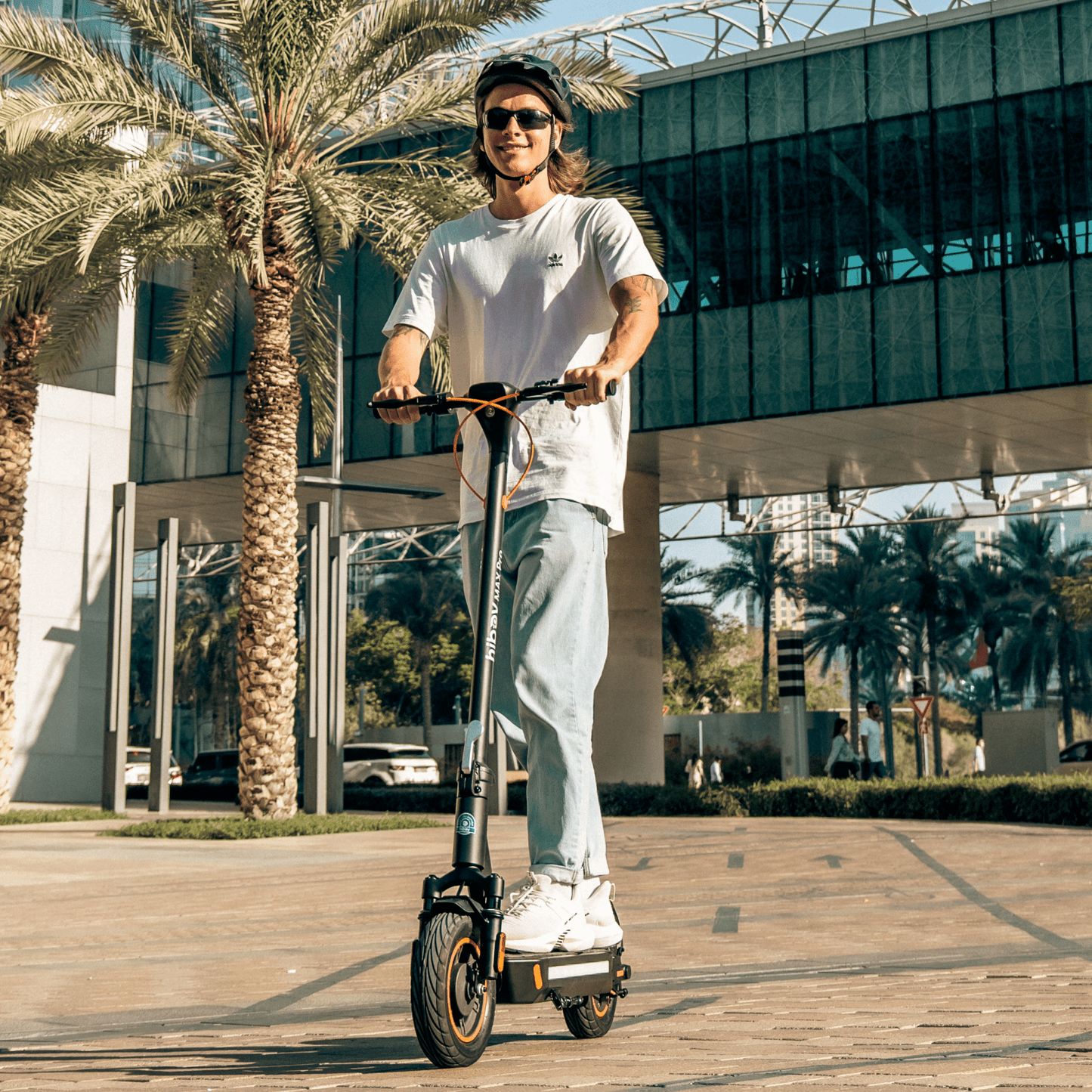 Person riding an electric scooter in a modern urban setting with palm trees.