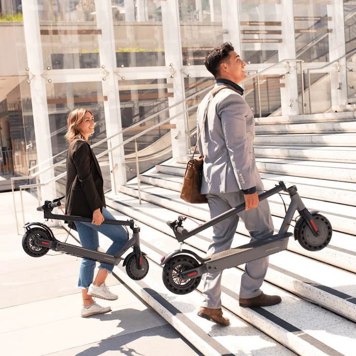 Two people walking with folded electric scooters on a modern urban staircase.