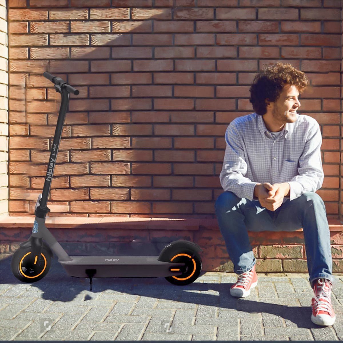Man sitting next to an electric scooter against a brick wall