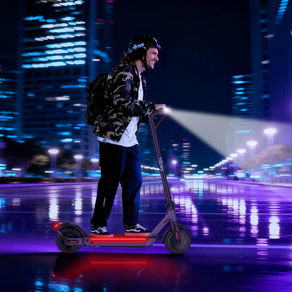 Person riding an electric scooter with a flashlight on a city street at night.