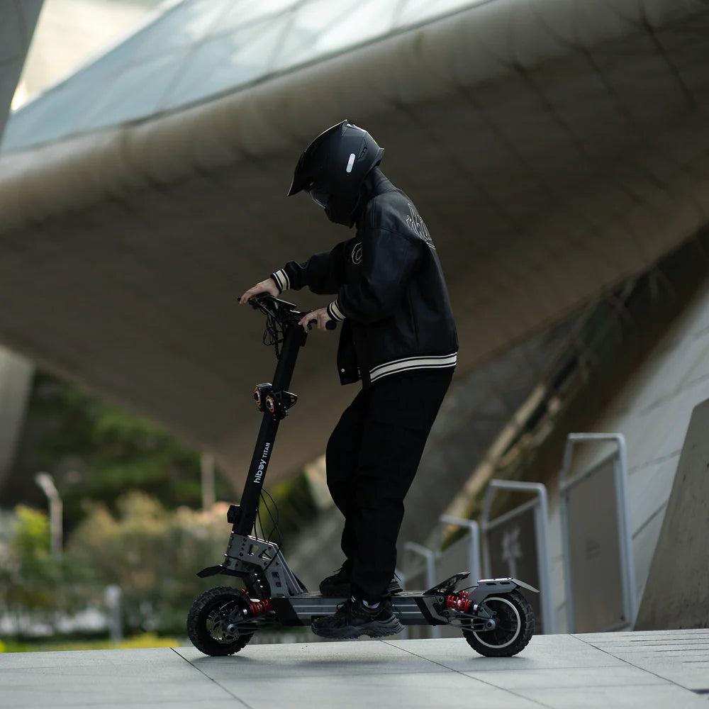 Person riding a scooter in an urban setting with modern architecture.