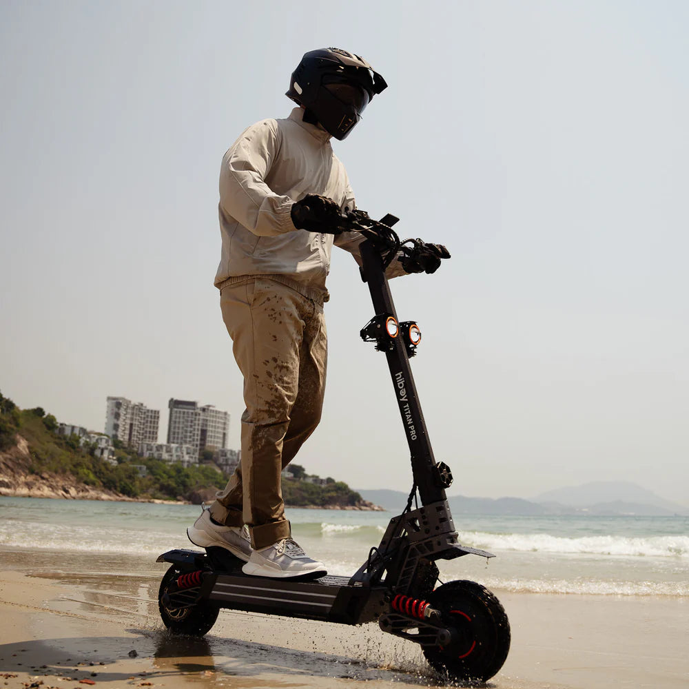 Person riding an electric scooter on a beach with buildings in the background