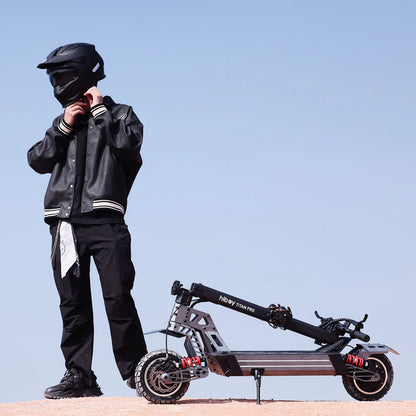 Person in black motorcycle gear standing next to a black electric scooter with a clear blue sky background