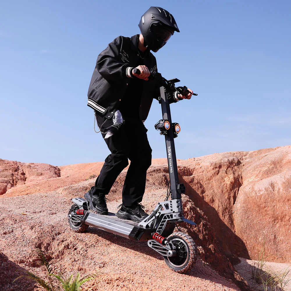 Person riding an electric scooter on rocky terrain with a clear blue sky.