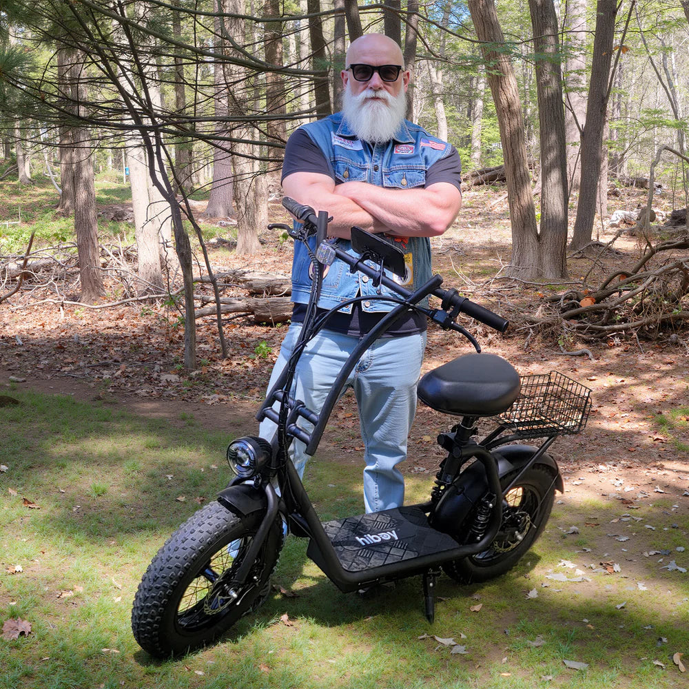 Man standing with a black electric scooter in a forest setting