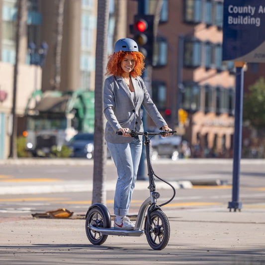 Woman riding a scooter on a city street with buildings and traffic lights in the background