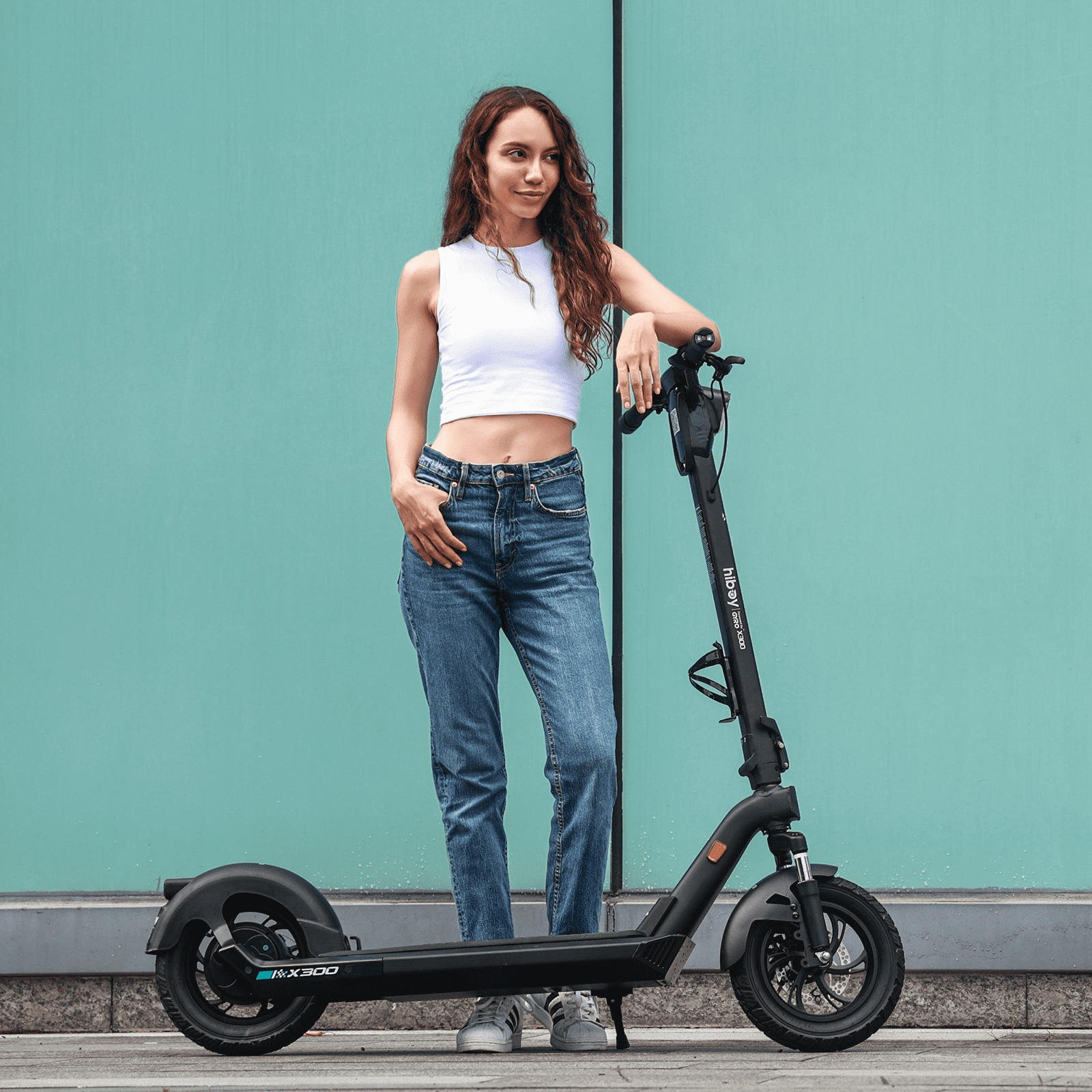 Woman standing next to a black electric scooter against a teal wall.