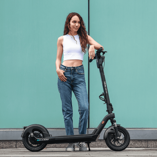 Woman standing next to a black electric scooter against a teal wall.