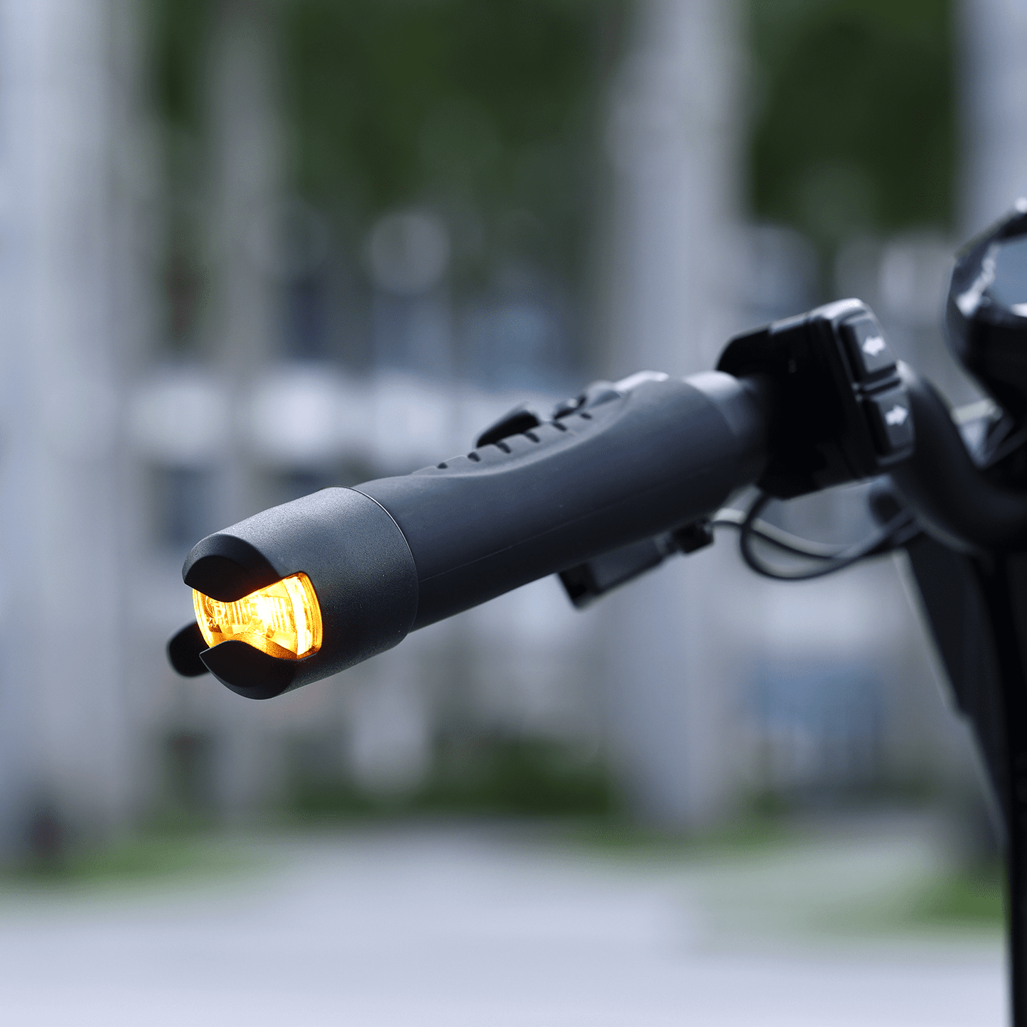 Close-up of a motorcycle handlebar with an illuminated turn signal against a blurred background