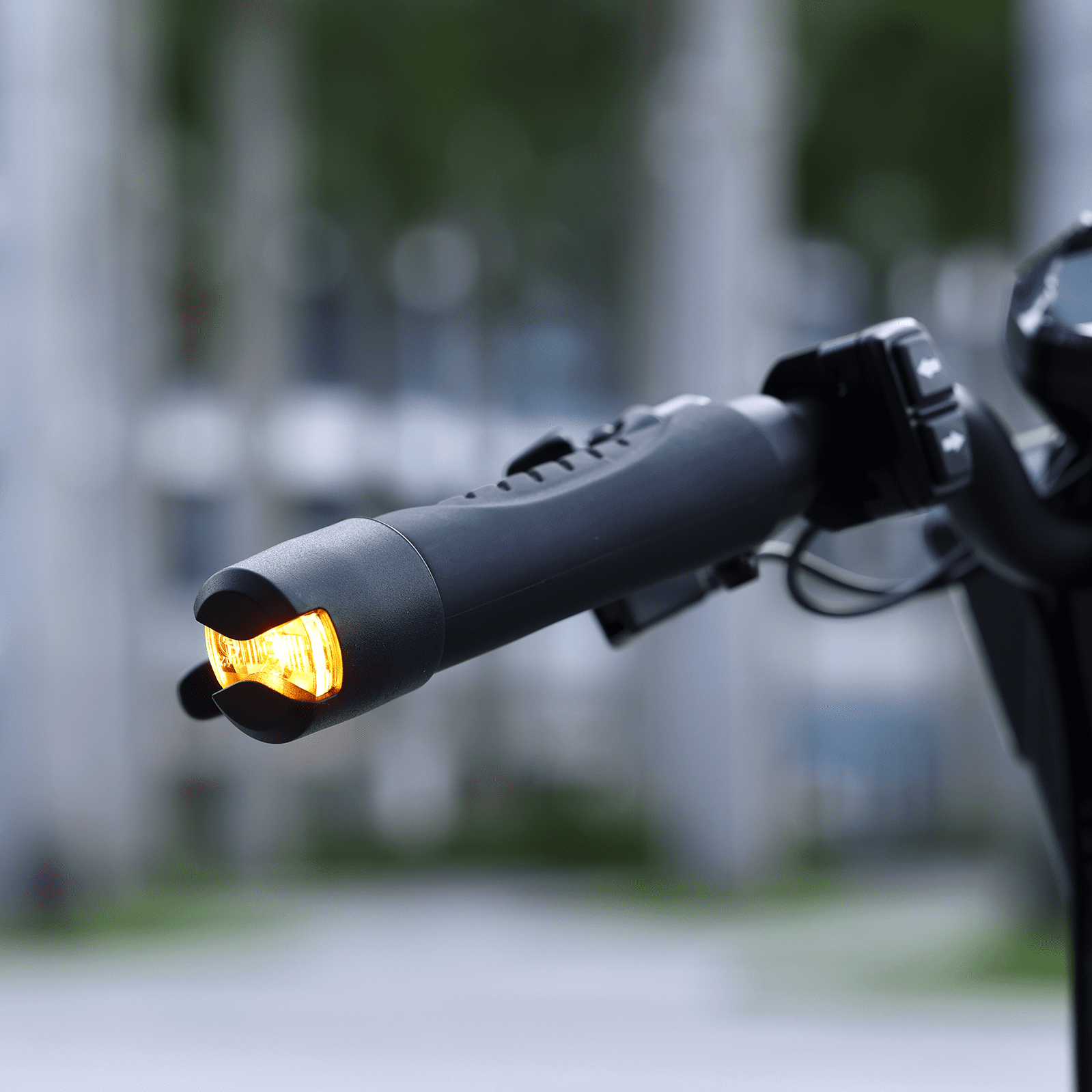 Close-up of a motorcycle handlebar with an illuminated turn signal against a blurred background