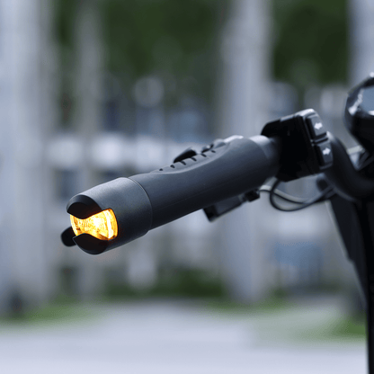 Close-up of a motorcycle handlebar with an illuminated turn signal against a blurred background