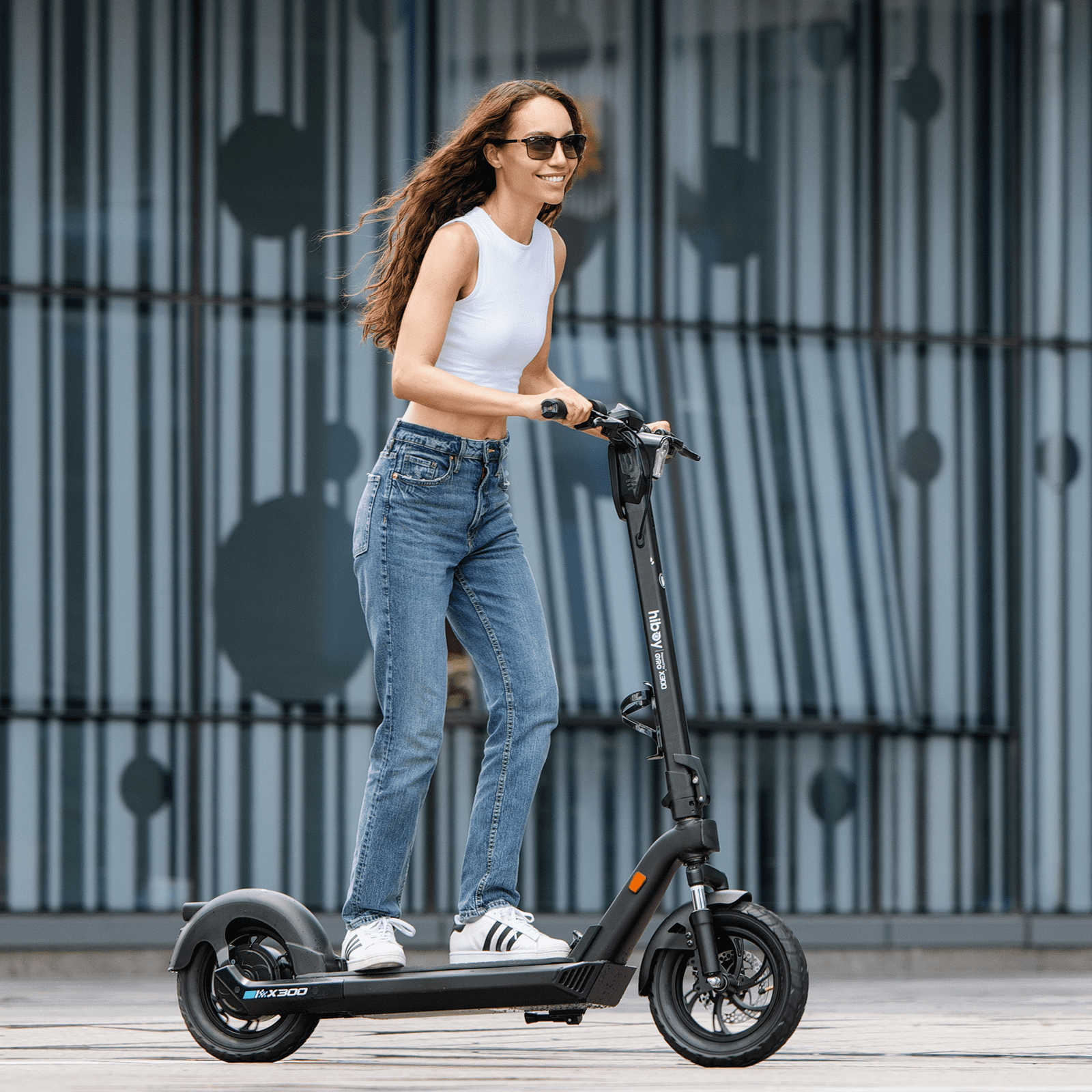 Woman riding an electric scooter on a wooden deck with a metal fence background