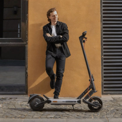 Man standing next to an electric scooter against a building wall.