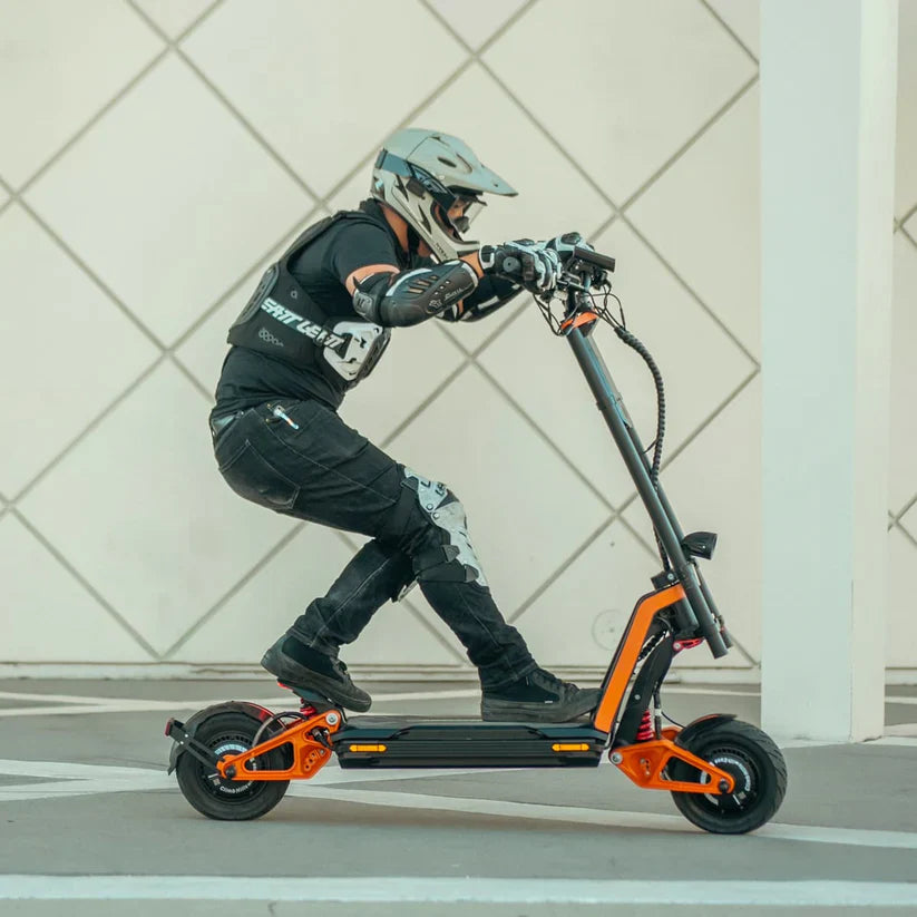 Person riding an electric scooter with a helmet and protective gear on a tiled floor.