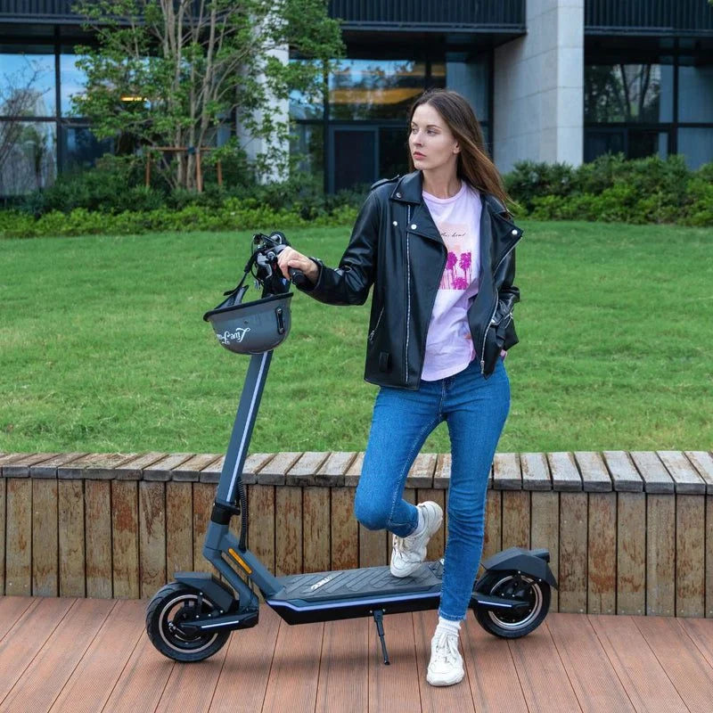Woman standing next to an electric scooter on a wooden deck with grass and building in the background