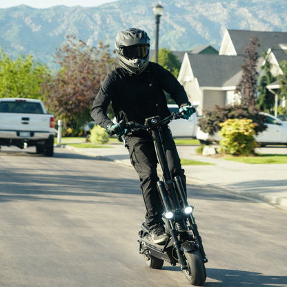 Person riding a black electric scooter on a residential street with mountains in the background