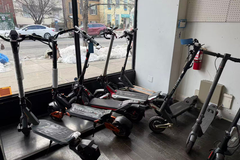 Multiple electric scooters displayed inside a store with a snowy street outside.