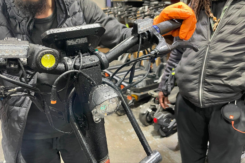 Two people working on a motorcycle in a workshop setting.