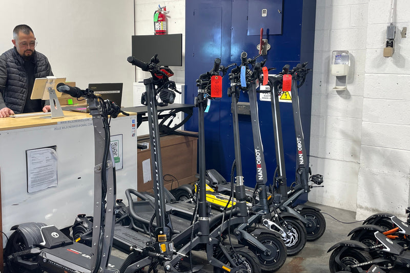 Row of electric scooters in a storage or maintenance area with a person in the background.
