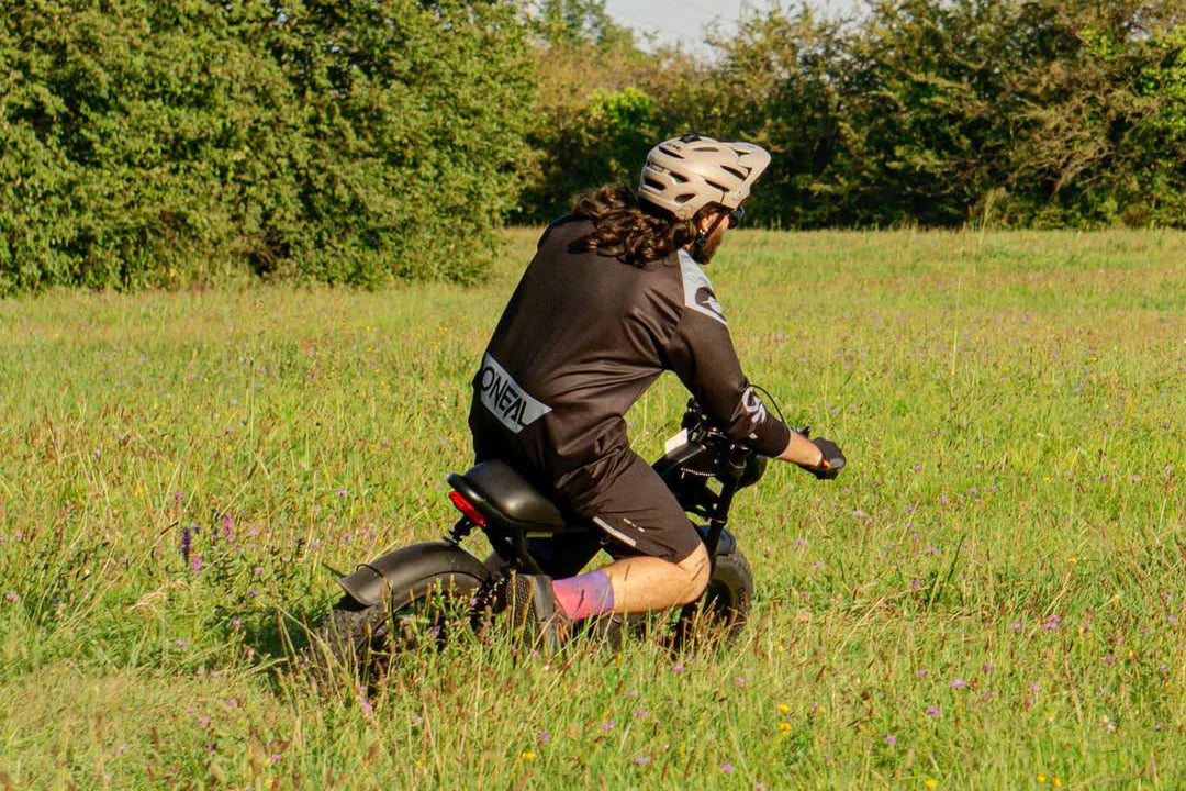 Person riding a balance bike in a grassy field with trees in the background