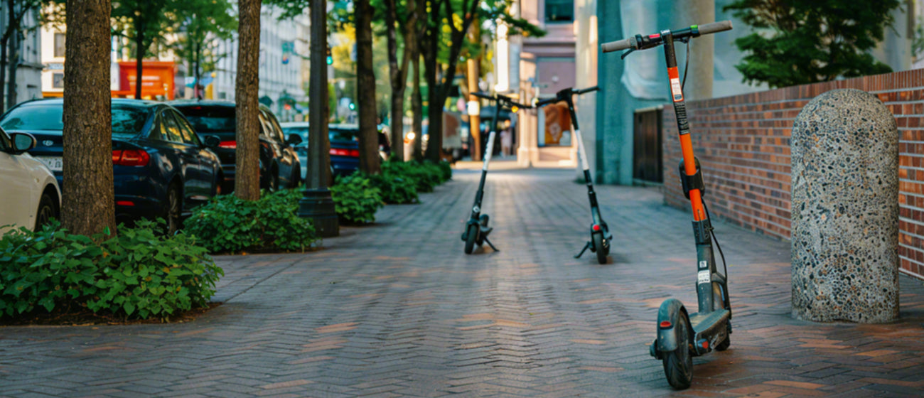 Electric scooters on a city sidewalk with buildings and trees in the background