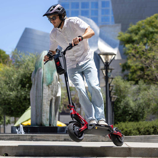 Person riding a red electric scooter in an urban setting with trees and buildings in the background.