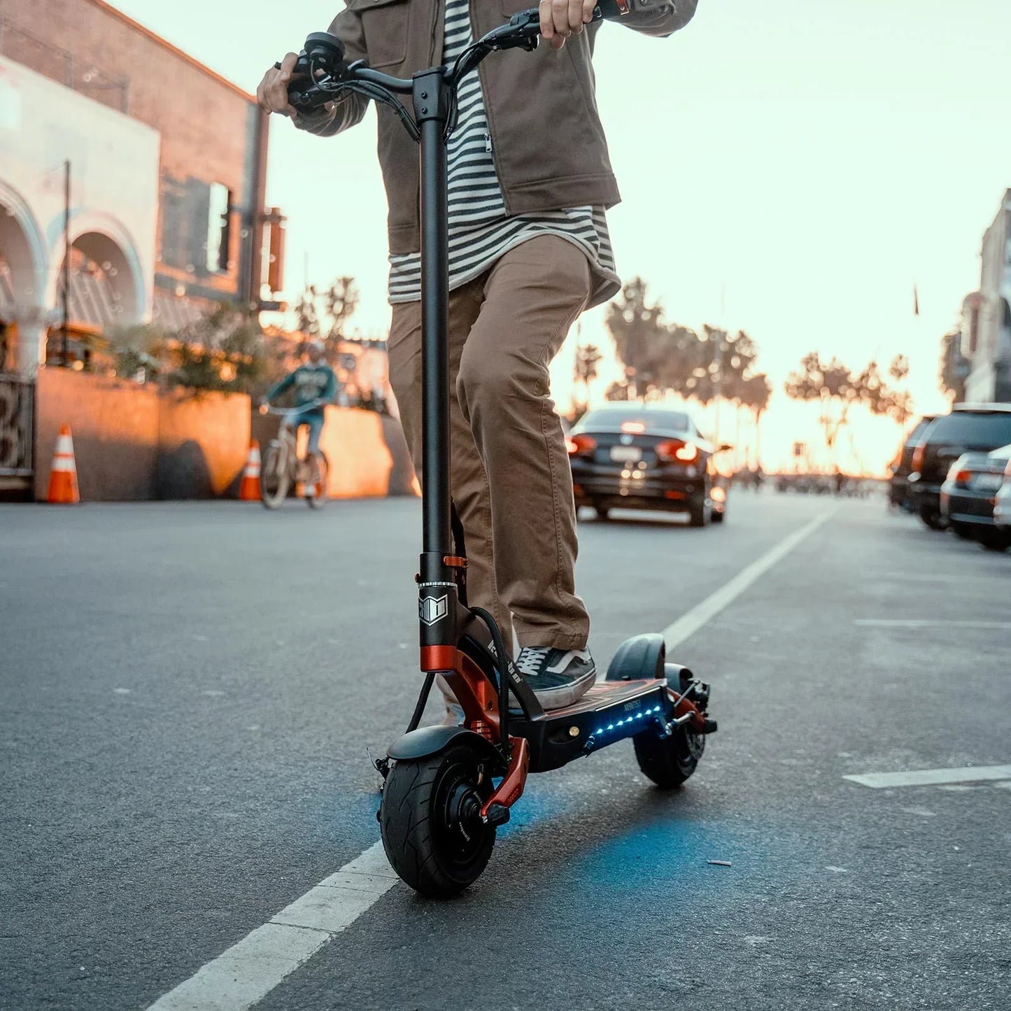 Person riding an electric scooter on a city street with buildings and cars in the background.
