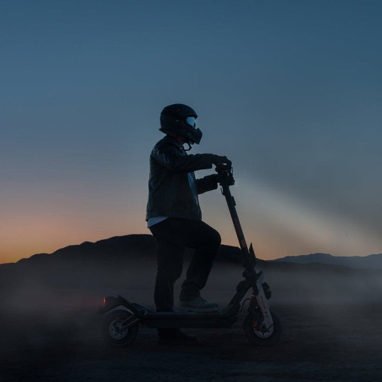 Person riding a scooter in a desert landscape at dusk
