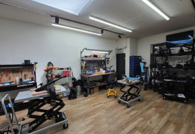 Workshop with various tools and equipment on wooden floors and white walls.