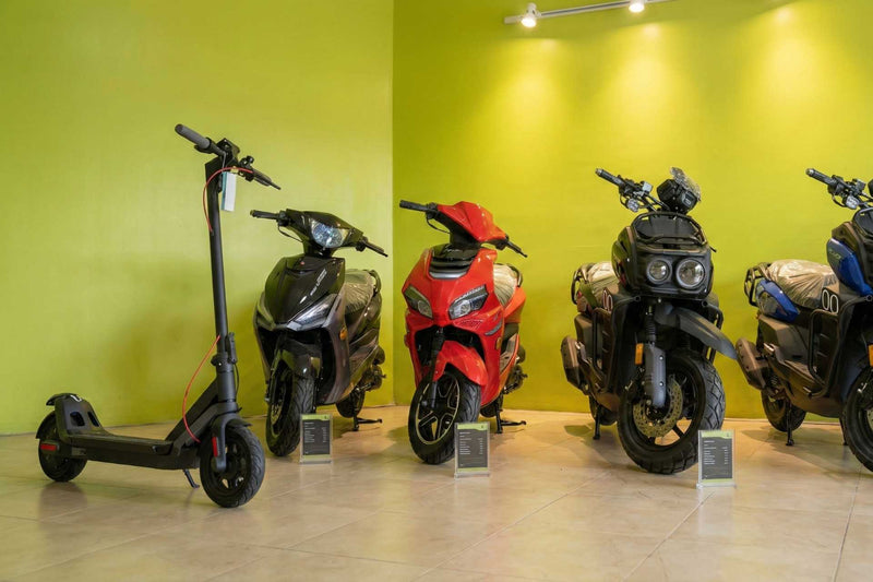Four motorcycles and a scooter on display against a green wall.